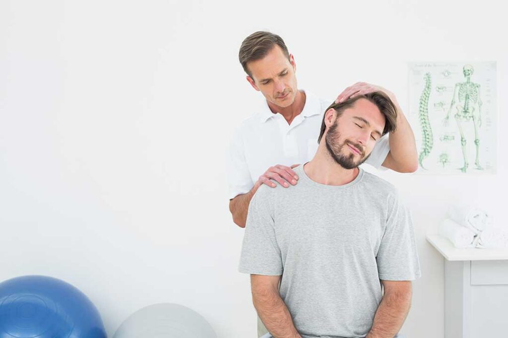 An adult applying a wrapped ice pack to their lower back while seated in a living room chair.