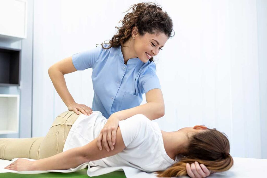 Older adult performing a gentle balance exercise beside a chair with guidance from a healthcare provider.